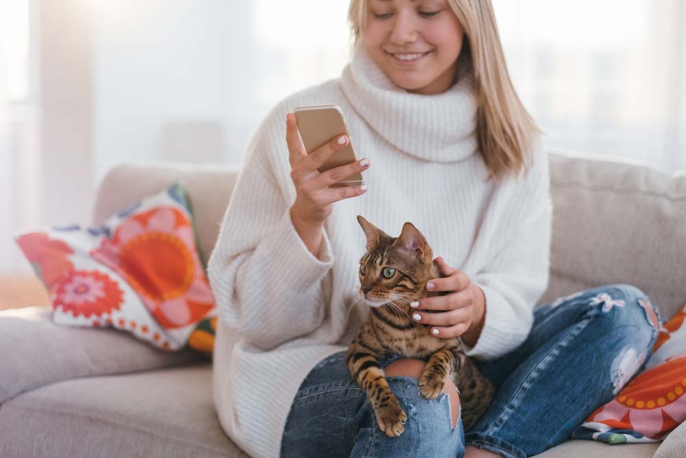 a woman holding a mobile phone with a cat sitting on her lap