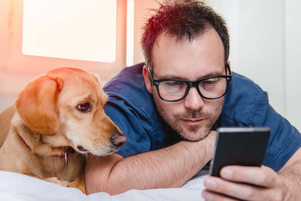 man sitting next to a dog and holding a mobile phone