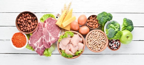 Uncooked food on a table including broccoli, beans, meat, and chicken